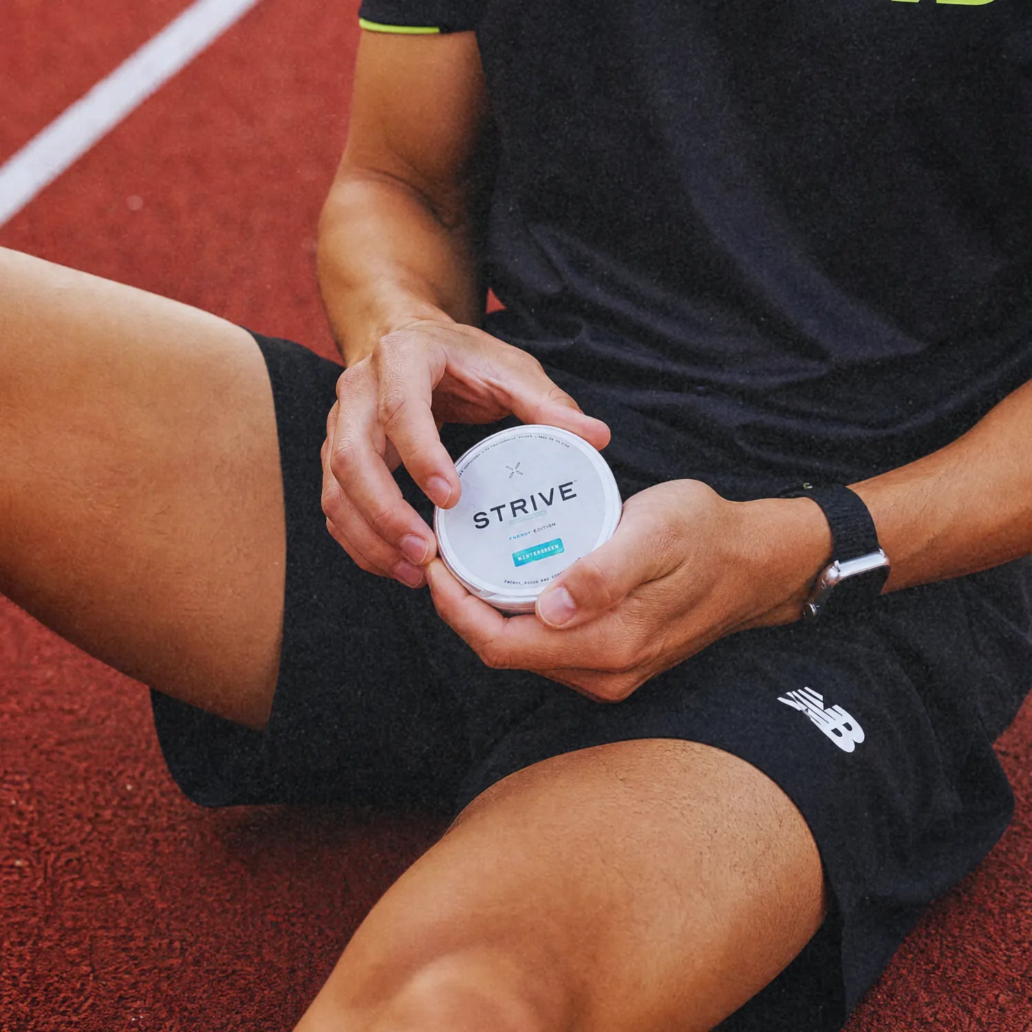 A runner seated on a track, holding a Strive can in both hands