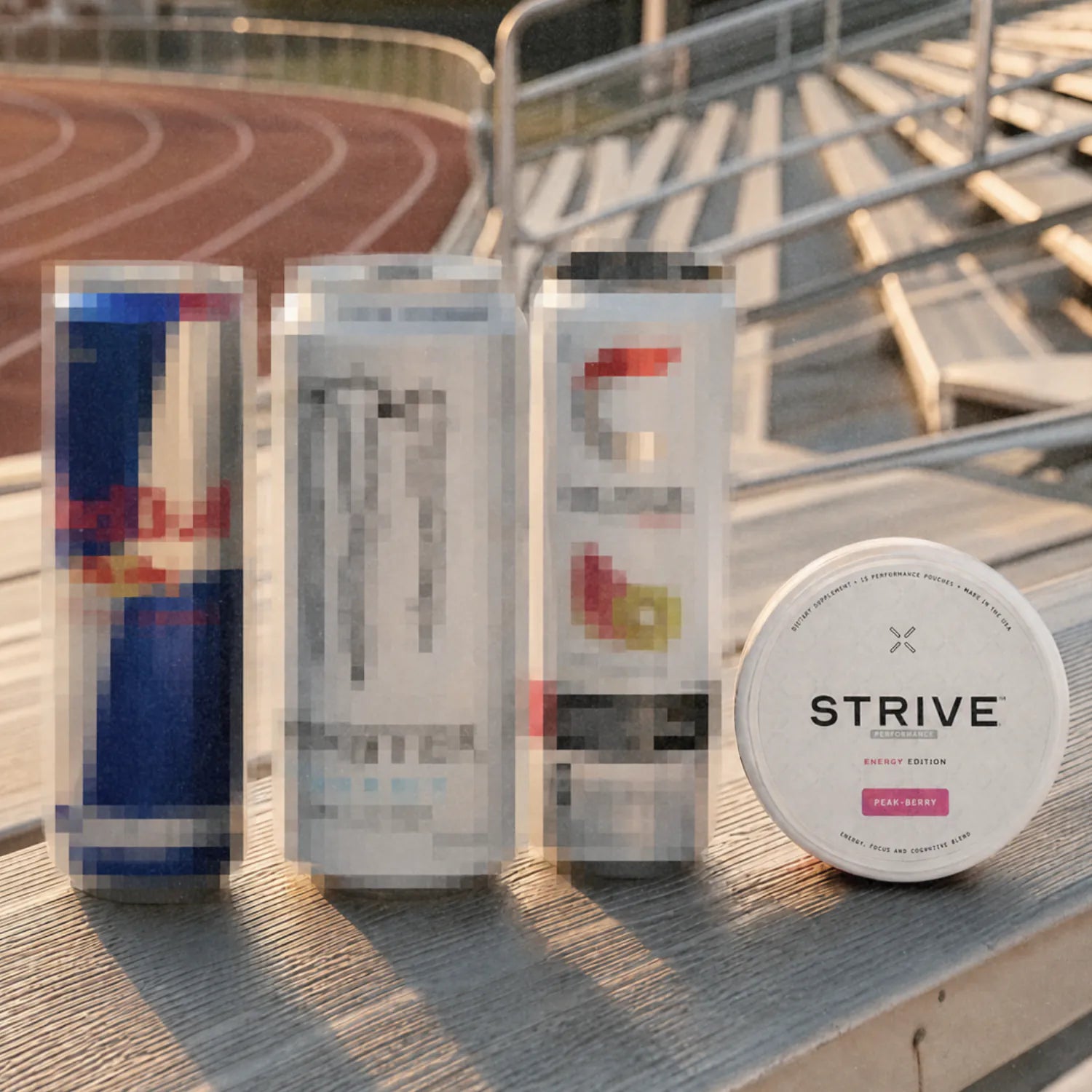 A Strive can on a bleacher bench beside three tall drink cans, a running track behind